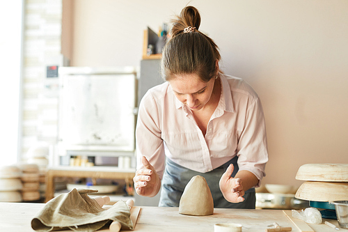 Waist up portrait of female potter shaping clay while working in studio, copy space