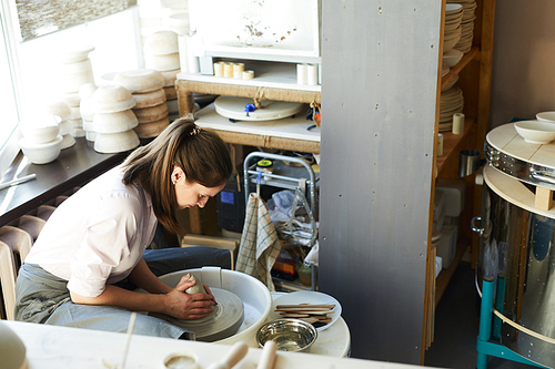 High angle portrait of female potter using wheel while working in studio, copy space