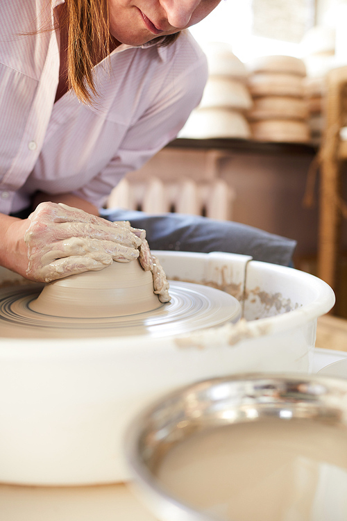 Side view portrait of unrecognizable female potter shaping clay on wheel while working in studio, copy space