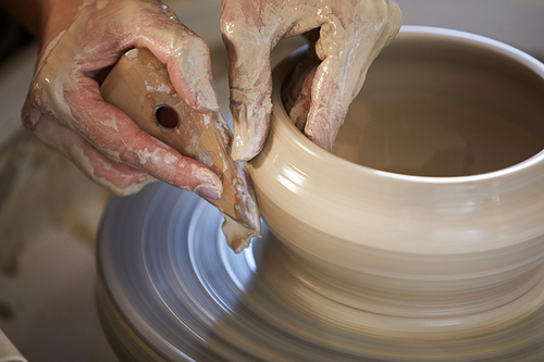 Close up of female hands shaping clay on potters wheel while working in studio, copy space