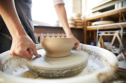Closeup of female artisan cutting clay pot off potters wheel using string, copy space