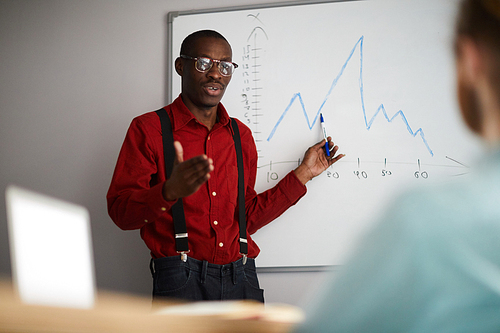 Waist up portrait of stylish African businessman standing by whiteboard and giving presentation in office, copy space