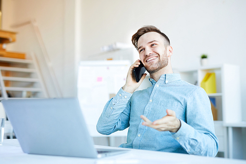 Portrait of handsome young man speaking by phone anile working in office and smiling happily, copy space