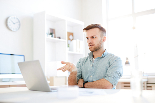 Portrait of puzzled man pointing at laptop screen with questioning look , copy space