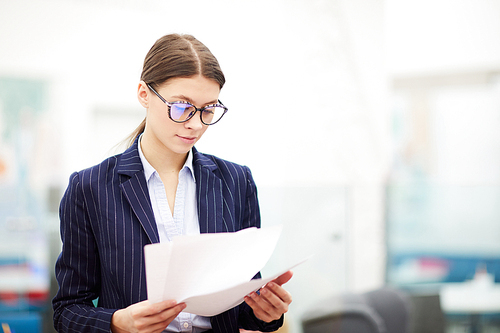 Waist up portrait of young businesswoman reading document standing in office, copy space