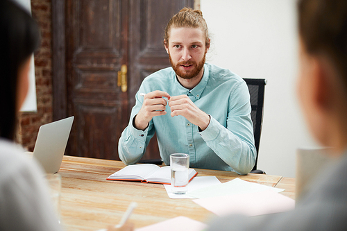 Portrait of contemporary bearded man talking to colleagues while discussing strategy at meeting table in office, copy space