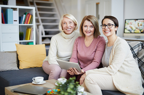 Portrait of three happy modern women  and smiling while using digital tablet at home, copy space