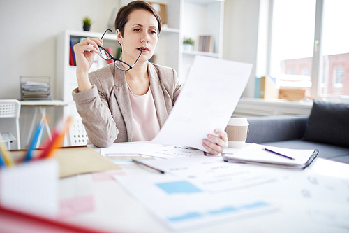 Portrait of confident businesswoman reading document sitting at workplace in office, copy space