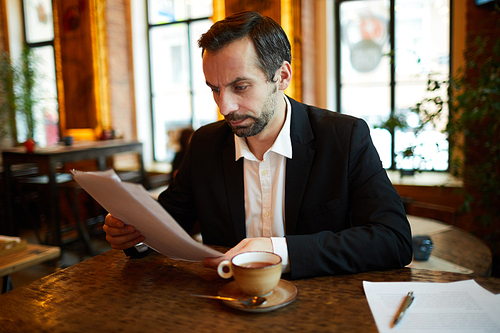 Portrait of handsome businessman working in cafe reading project documentation, copy space