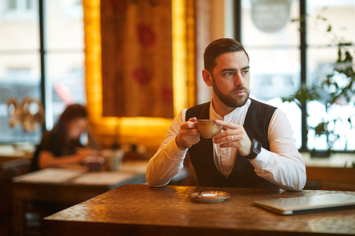 Portrait of pensive businessman drinking coffee in cafe and looking away, copy space
