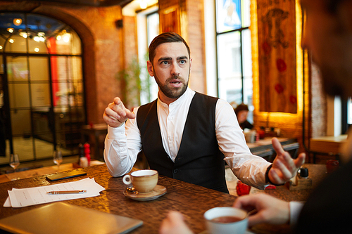 Portrait of mature businessman talking to partner during meeting in cafe and gesturing actively, copy space