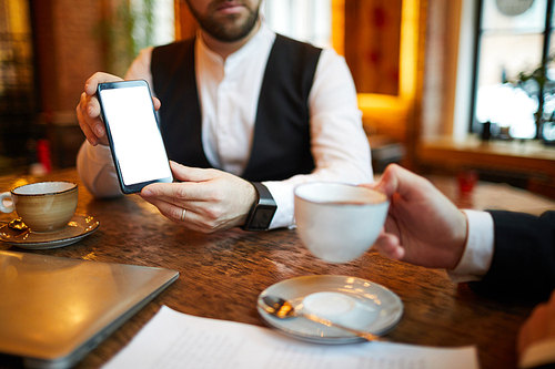 Closeup of unrecognizable businessman showing smartphone with blank screen during meeting in cafe, copy space