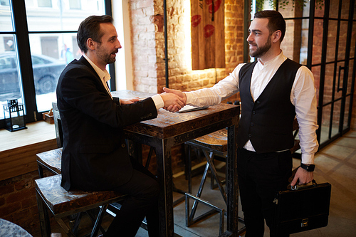 Side view portrait of two business partners shaking hands  during meeting in cafe, copy space