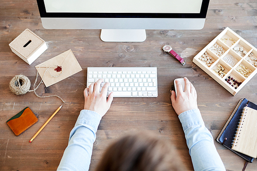 High angle view of unrecognizable graphic designer in shirt sitting at table with accessories and using computer while working on web project