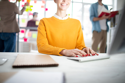 Young casual businesswoman with red manicure touching keys of keypad while working in the net by workplace