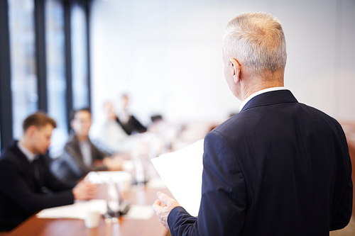 Back view portrait of senior businessman giving speech in conference room talking to employees, copy space