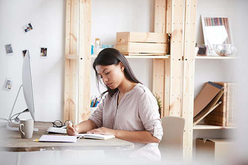 Portrait of young mixed race woman working or studying sitting at desk in home office, copy space