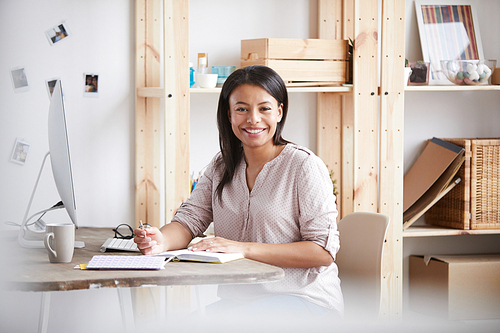 Portrait of young mixed race woman smiling happily while working or studying sitting at desk in home office, copy space