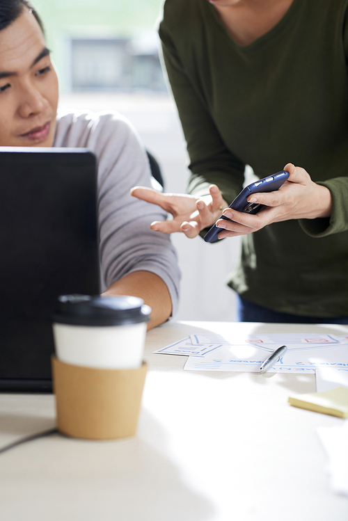 Irritated woman gesturing hand and showing mistake on smartphone while talking to colleague about new design for mobile app