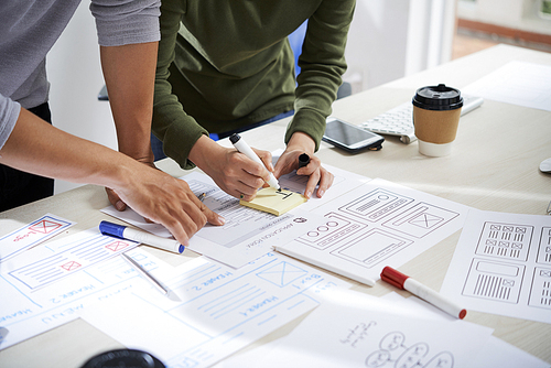 Hands of UX designers discussing documents and working on website wireframe design