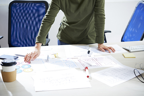 Close-up of unrecognizable creative software engineer standing at desk with sketches, markers and stickers and developing user-friendly mobile app