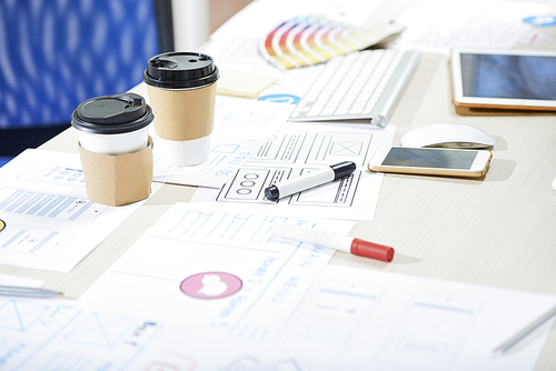 Mess on desk of ux designer: close-up of office table with takeout coffee cups, colorful felt-tip pens, gadgets, sketches and schemes