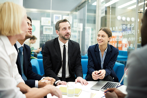 Group of cheerful business people discussing ideas for startup project sitting at coffee table in office, copy space