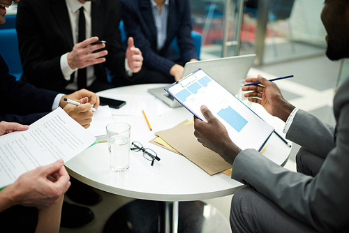 Mid section crop of unrecognizable business people meeting in office, focus on African man holding clipboard, copy space