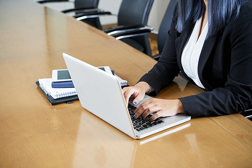 Business lady sitting at big meeting table and working on laptop in office
