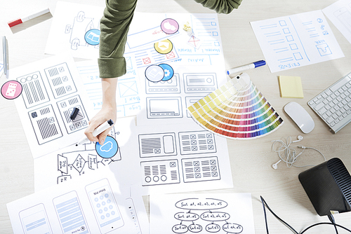 Wireframes of future project, paper samples of icons and color palette on table of UI designer