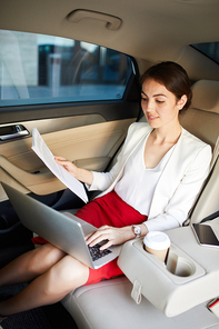 Portrait of successful businesswoman working in car using laptop in back seat, copy space