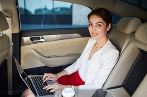 Portrait of successful businesswoman  and working in car using laptop in back seat, copy space