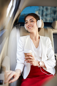 Portrait of young businesswoman listening to music in taxi and smiling happily