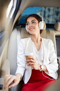 Portrait of young businesswoman listening to music in taxi and smiling happily looking at window