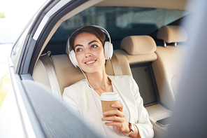 Portrait of beautiful young woman listening to music in taxi and smiling happily looking at window, copy space