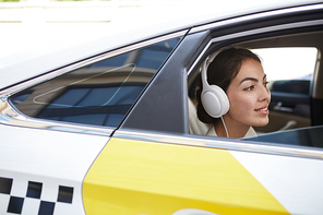 Side view portrait of beautiful young woman listening to music and looking at window in taxi, copy space