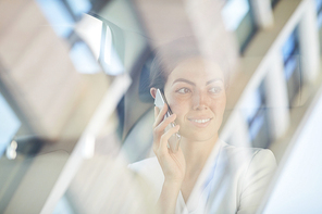 Portrait of young businesswoman speaking by smartphone in taxi shot from behind glass, copy space