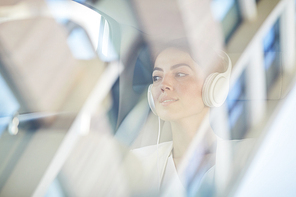 Portrait of young businesswoman listening to music in taxi shot from behind glass, copy space