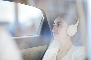 Side view portrait of young businesswoman listening to music in taxi shot from behind glass, copy space