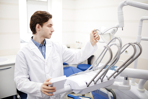 Waist up portrait of young dentist setting up equipment and dental chair in office, copy space