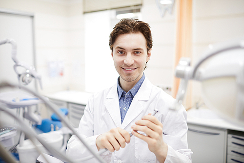Waist up portrait of smiling dentist  while posing in office holding bur machine, copy space