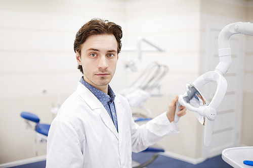 Waist up portrait of young dentist  while setting up equipment in office, copy space