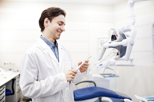 Side view portrait of young dentist setting up equipment in office and smiling, copy space