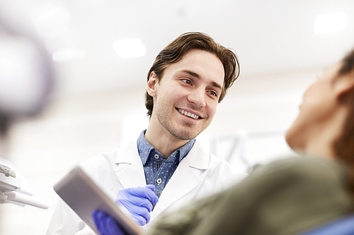 Low angle portrait of young dentist smiling cheerfully while consulting female patients, copy space