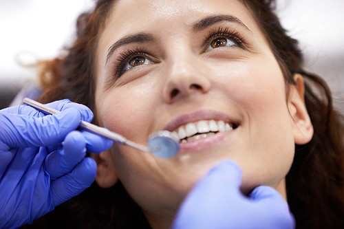 Closeup portrait of beautiful young woman lying in dental chair and smiling during consultation, copy space
