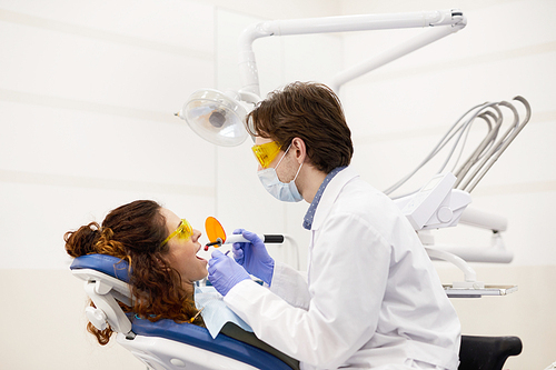 Side view portrait of young dentist treating patient during teeth whitening procedure in office, copy space