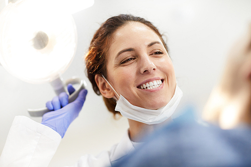 Low angle portrait of female dentist smiling happily looking at patients after checkup, copy space
