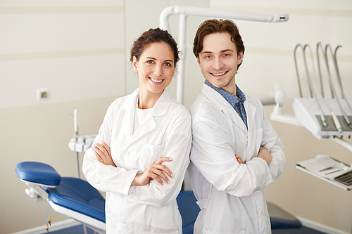 Waist up portrait of two confident dentists smiling at camera while posing with arms crossed, copy space