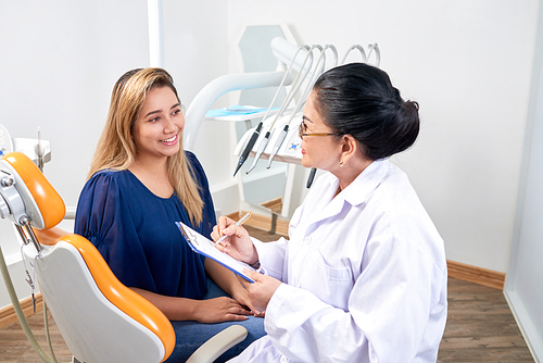 Pretty young woman talking to mature experienced dentist during annual check-up