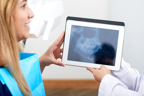 Dentist showing jaw x-ray on tablet computer to smiling female patient